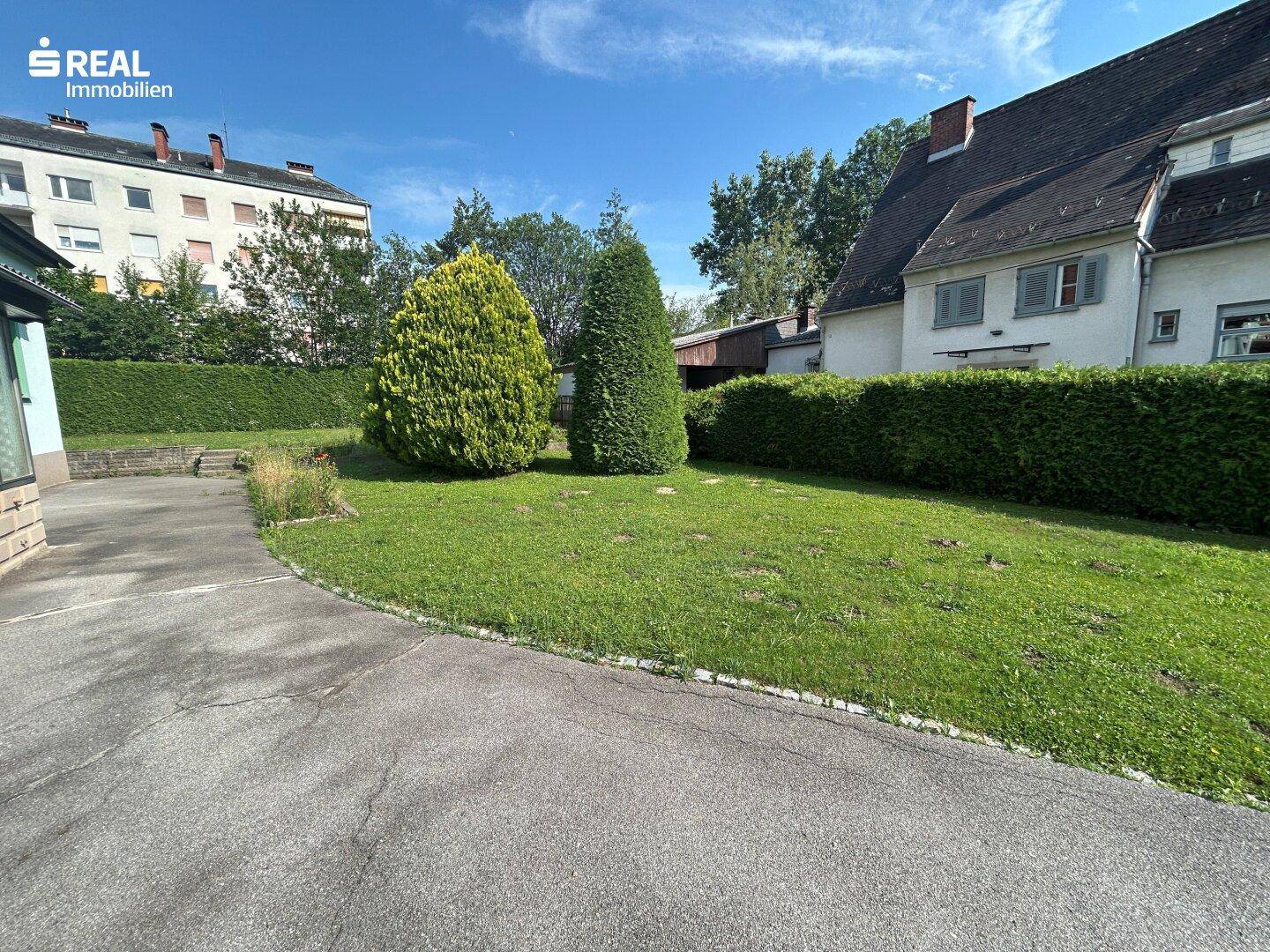 Großer, gepflegter Gartenbereich mit Rasenfläche, Zierbäumen und einer hohen Hecke.