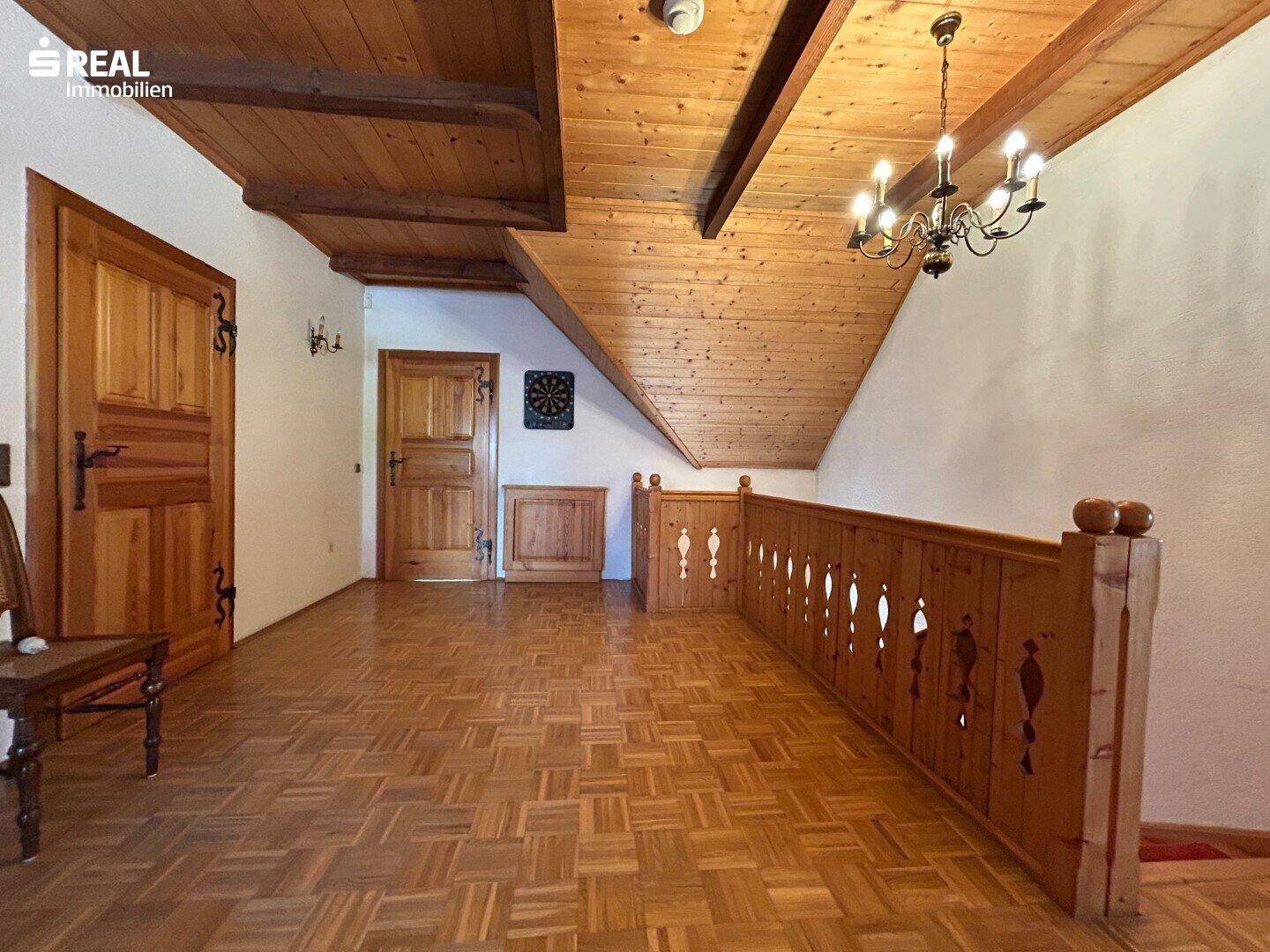 Heller Flur im Obergeschoss mit Parkettboden, sichtbaren Holzbalken und einer rustikalen Holzbrüstung.