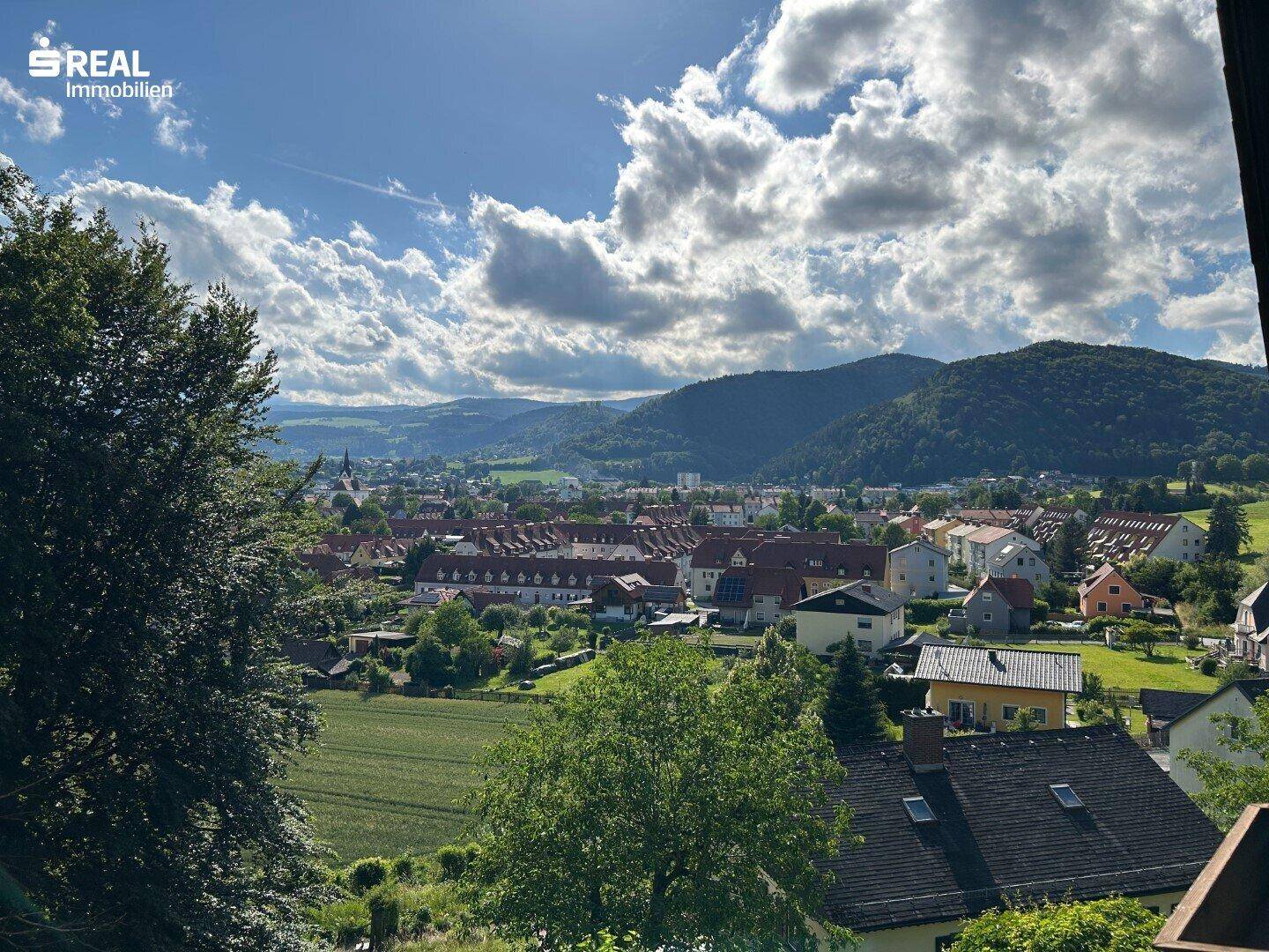 Weitläufiger Panoramablick über eine Stadt im Tal mit umliegenden Bergen unter blauem Himmel.