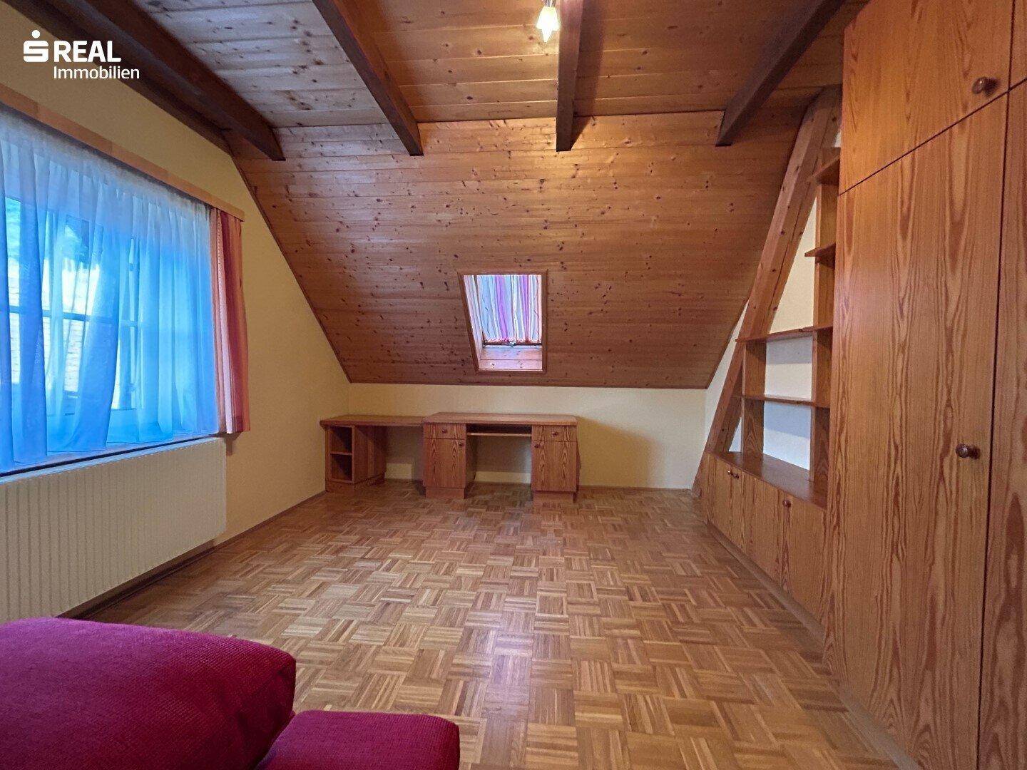 Geräumiges Schlafzimmer im Dachgeschoss mit Holzdecke, Parkettboden, Einbauschränken und Dachfenster.