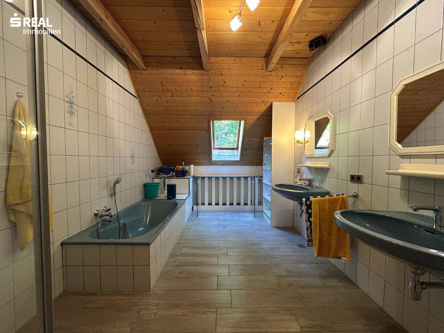 Dachgeschoss-Badezimmer mit Holzdecke, sichtbaren Balken, zwei Waschbecken, Badewanne und Dusche.