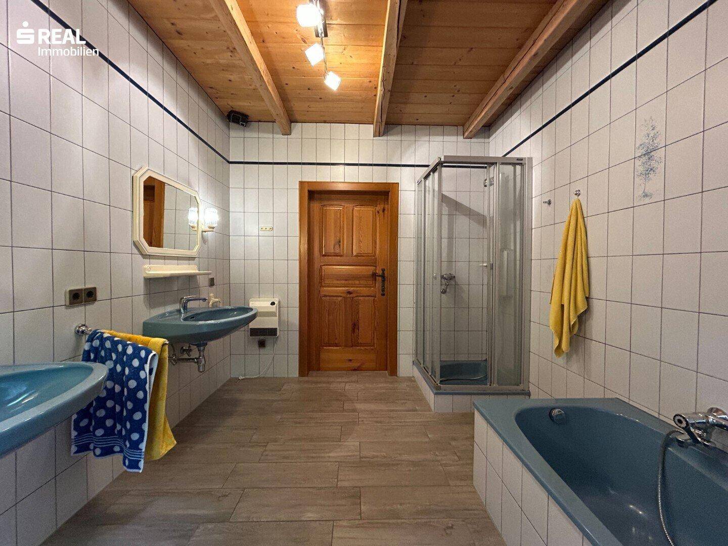 Weiterer Blick ins Dachgeschoss-Badezimmer mit Duschkabine, zwei Waschbecken und Holztür.
