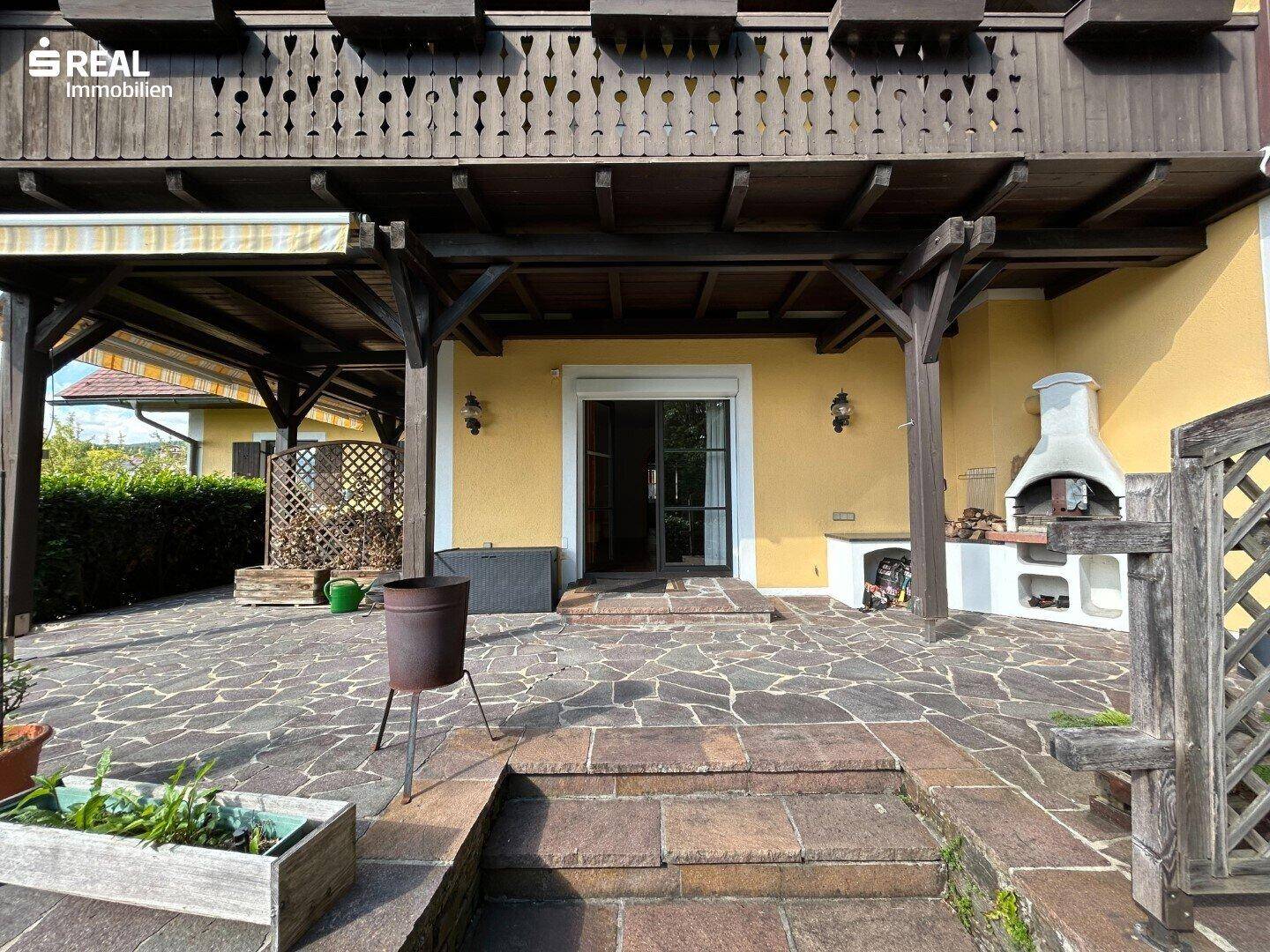 Große Außenterrasse mit Steinplattenboden, einem Außenkamin und direktem Zugang zum Haus.