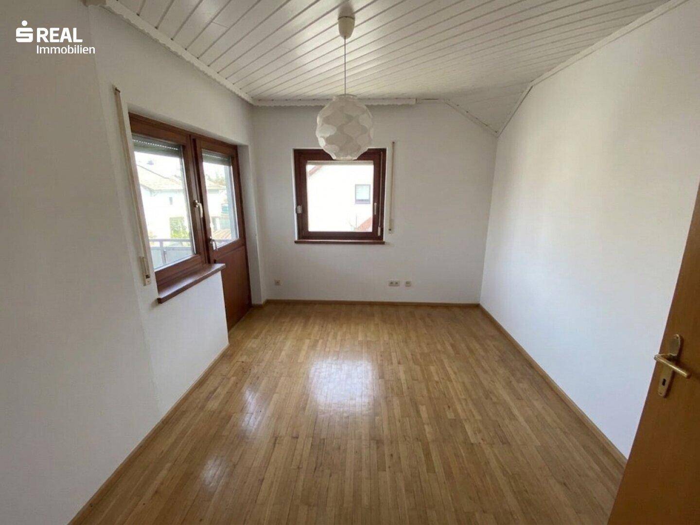Leeres Zimmer mit Laminatboden, weißen Wänden und einem Fenster mit Rollladen.