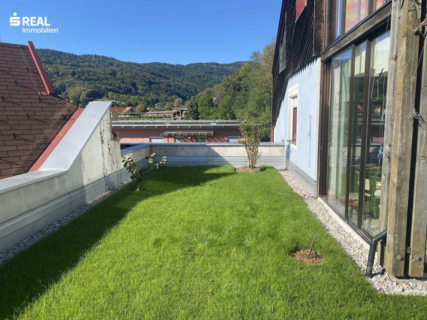 Grüner Rasenbereich mit Blick auf die umliegenden Berge und die Landschaft unter blauem Himmel.