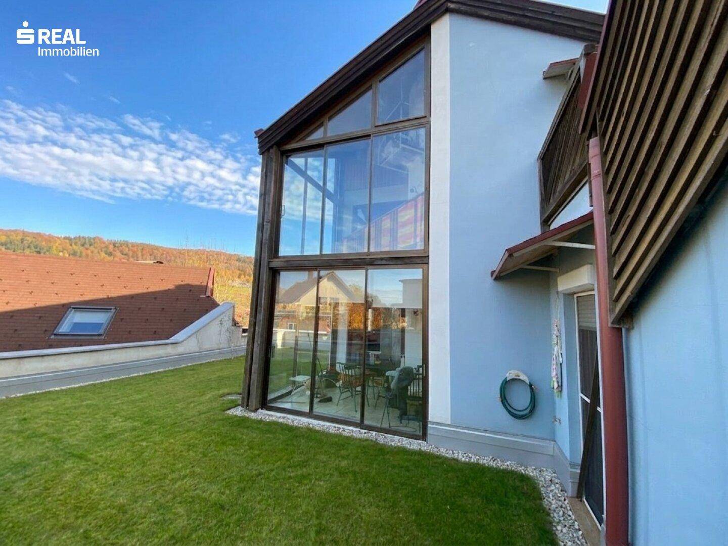 Moderne Hausfassade mit großen Glasflächen und einem gepflegten Rasen im Vordergrund.
