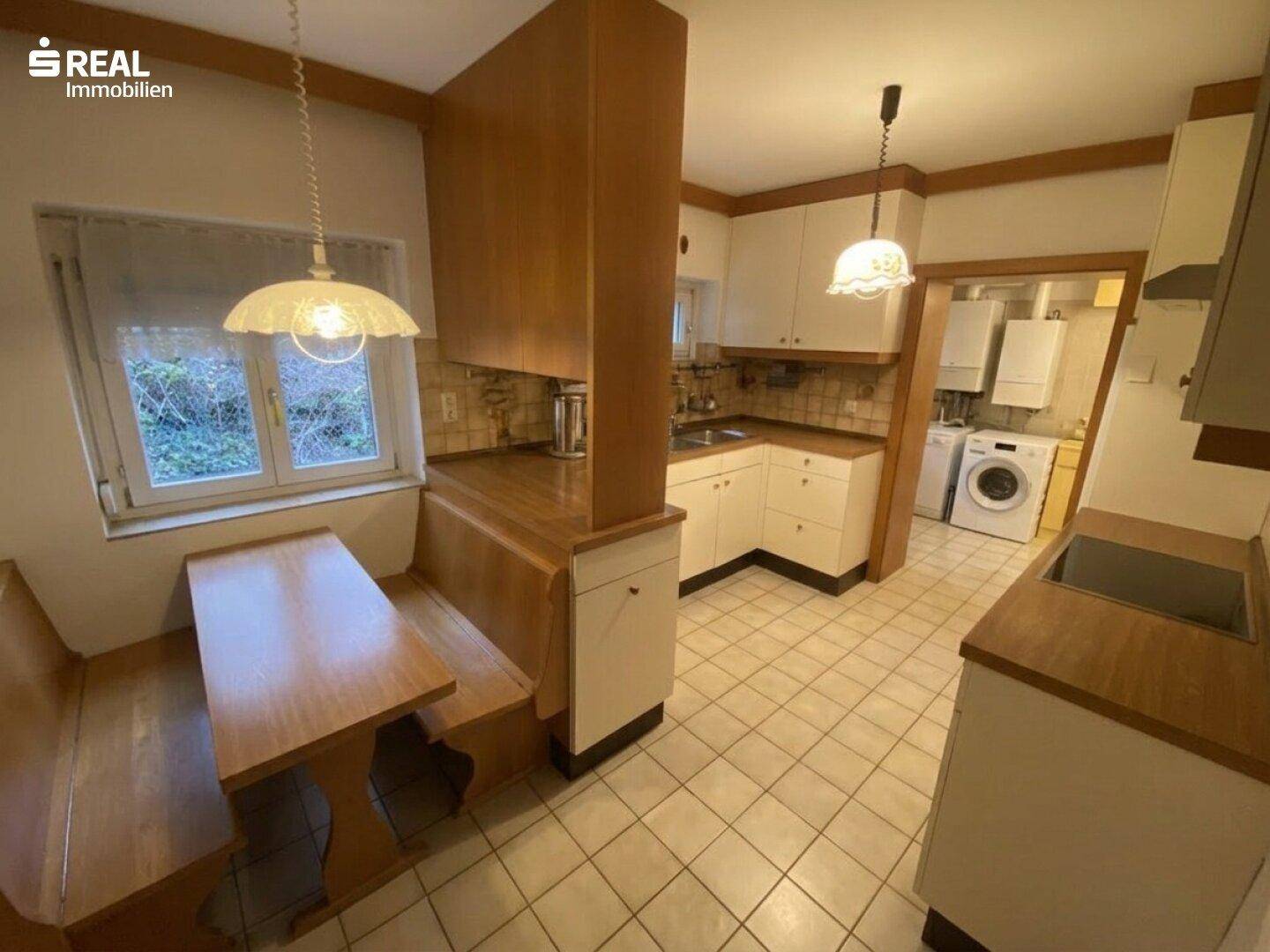Gemütliche Wohnküche mit Einbaubank, Holztheke und Fliesenboden, inklusive Waschmaschine.