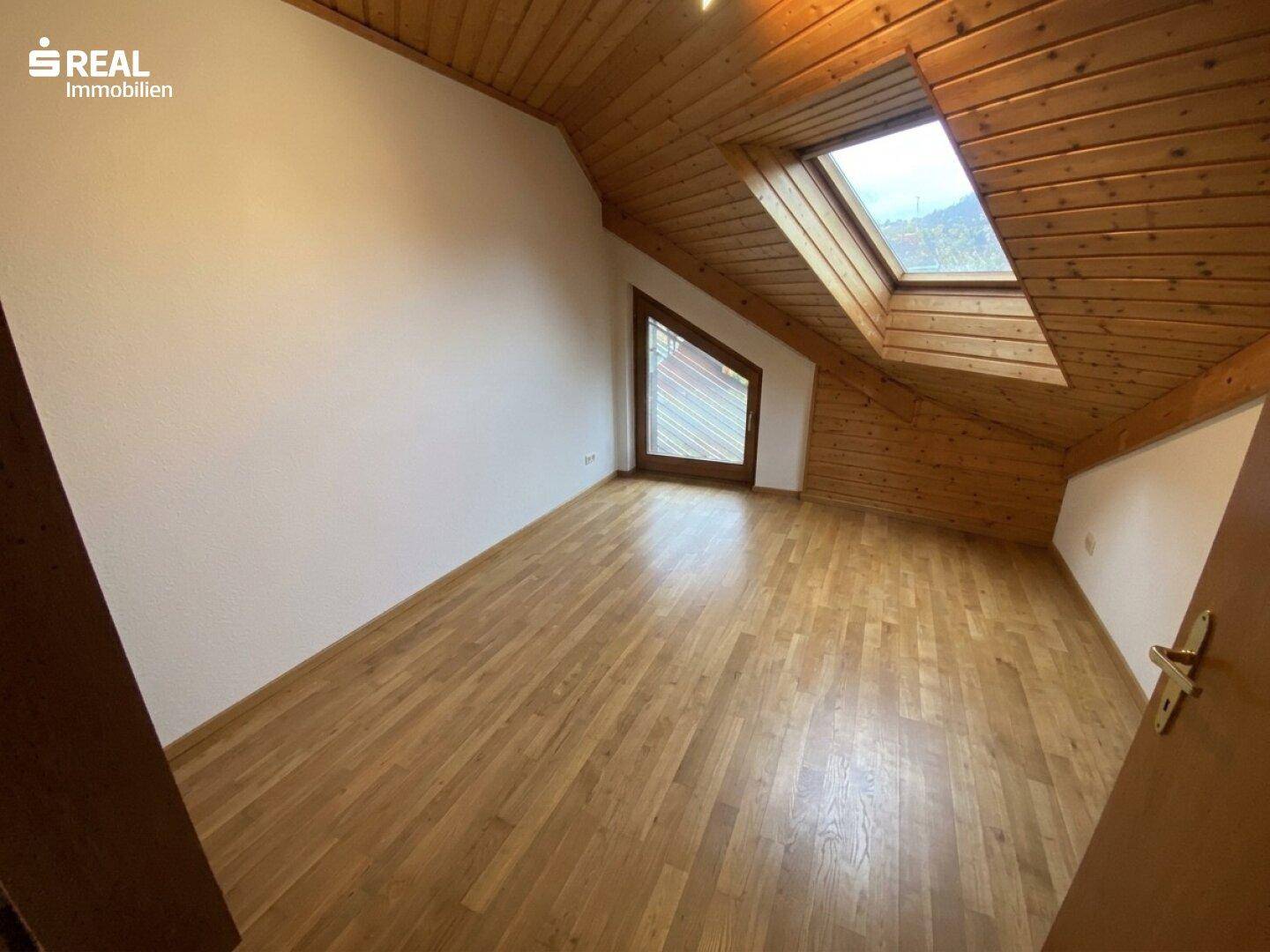 Geräumiges Zimmer mit Holzboden, Dachschräge und großem Dachfenster für viel Tageslicht.