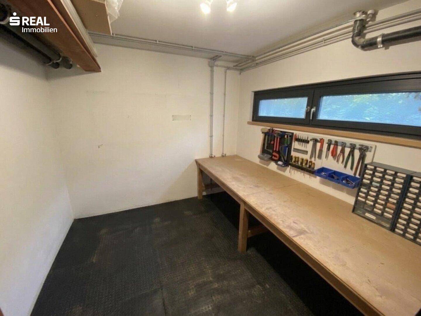 Werkstattraum im Keller mit Werkbank, Werkzeugen und kleinem Fenster für Tageslicht.