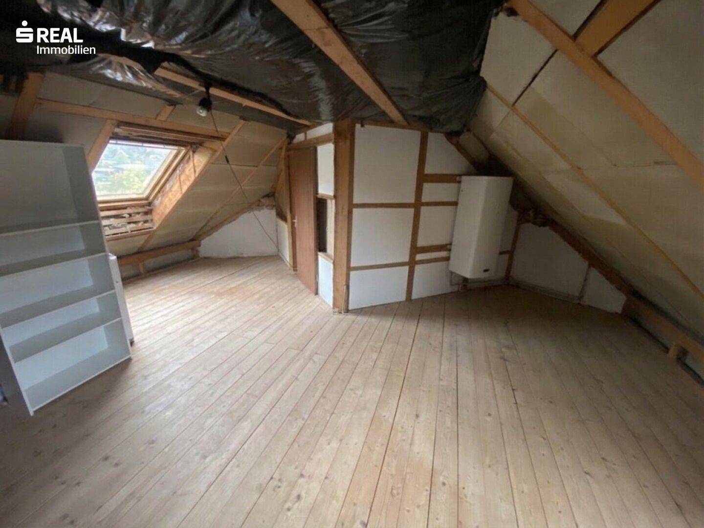 Ausbaufähiger Dachboden mit Holzboden, Dachschräge und Dachfenster für zukünftige Nutzung.