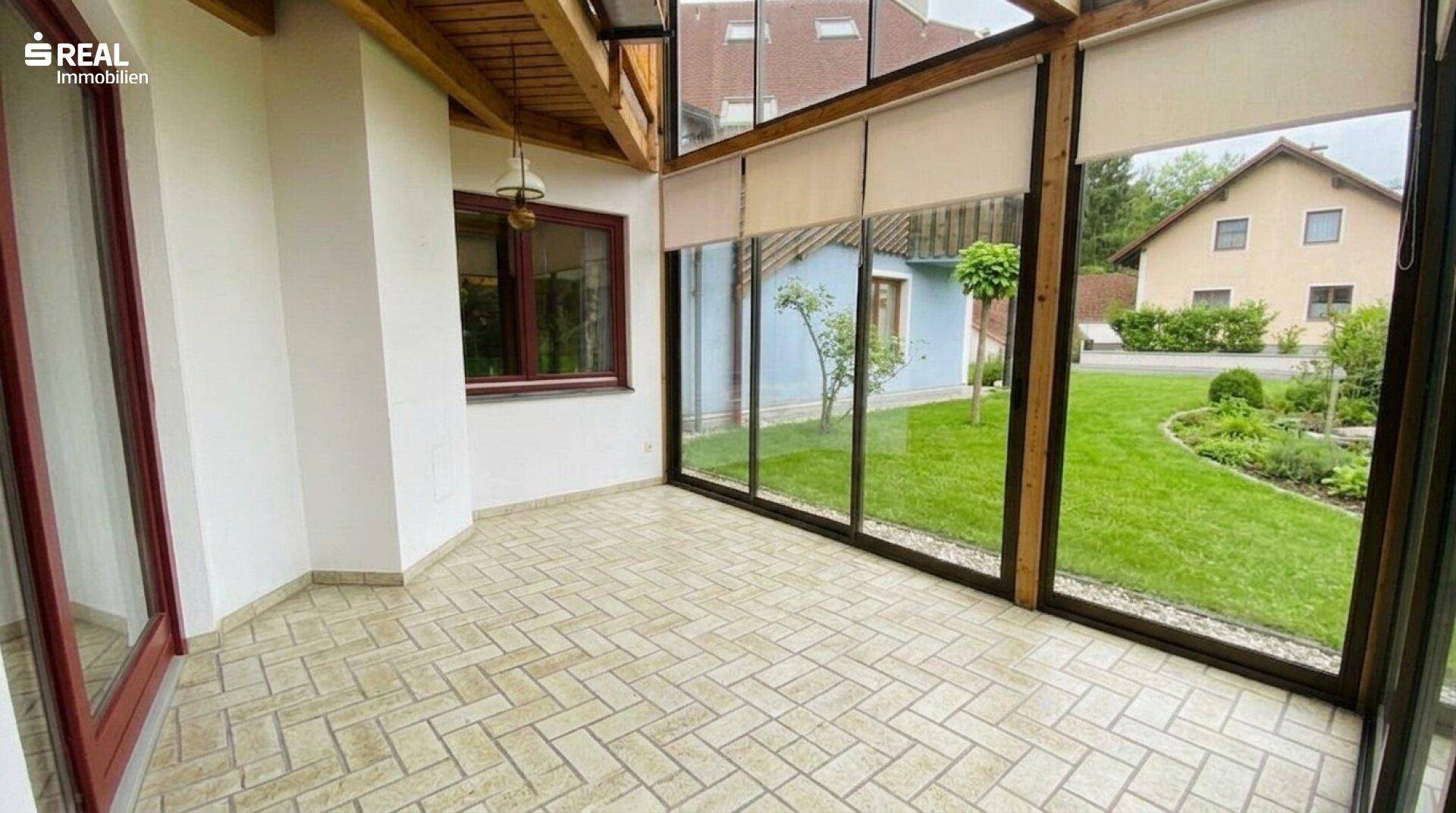 Heller Wintergarten mit Fliesenboden und großen Glasfronten zum Garten, ideal für Entspannung.