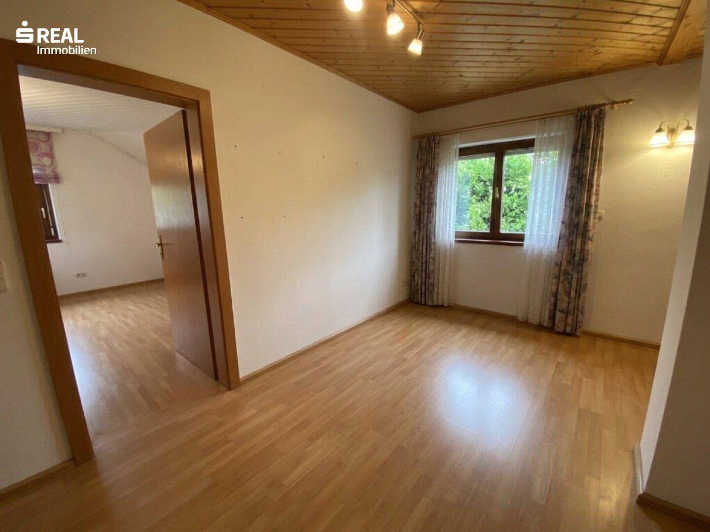 Helles Zimmer mit Holzboden und Fenster mit Blick ins Grüne, ideal zum Entspannen.