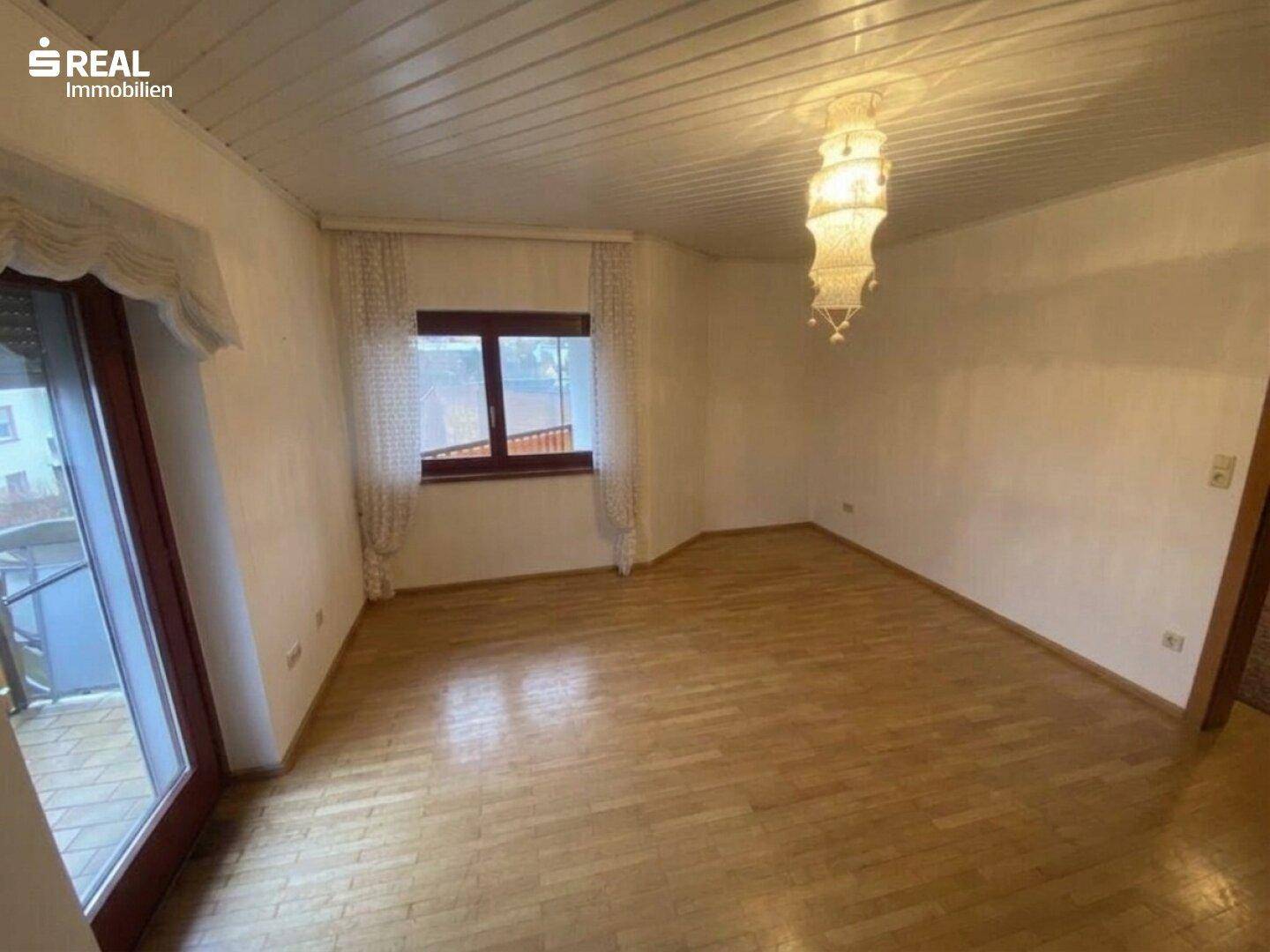 Geräumiges Zimmer mit Holzboden, großer Fensterfront und Zugang zu einem Außenbereich.