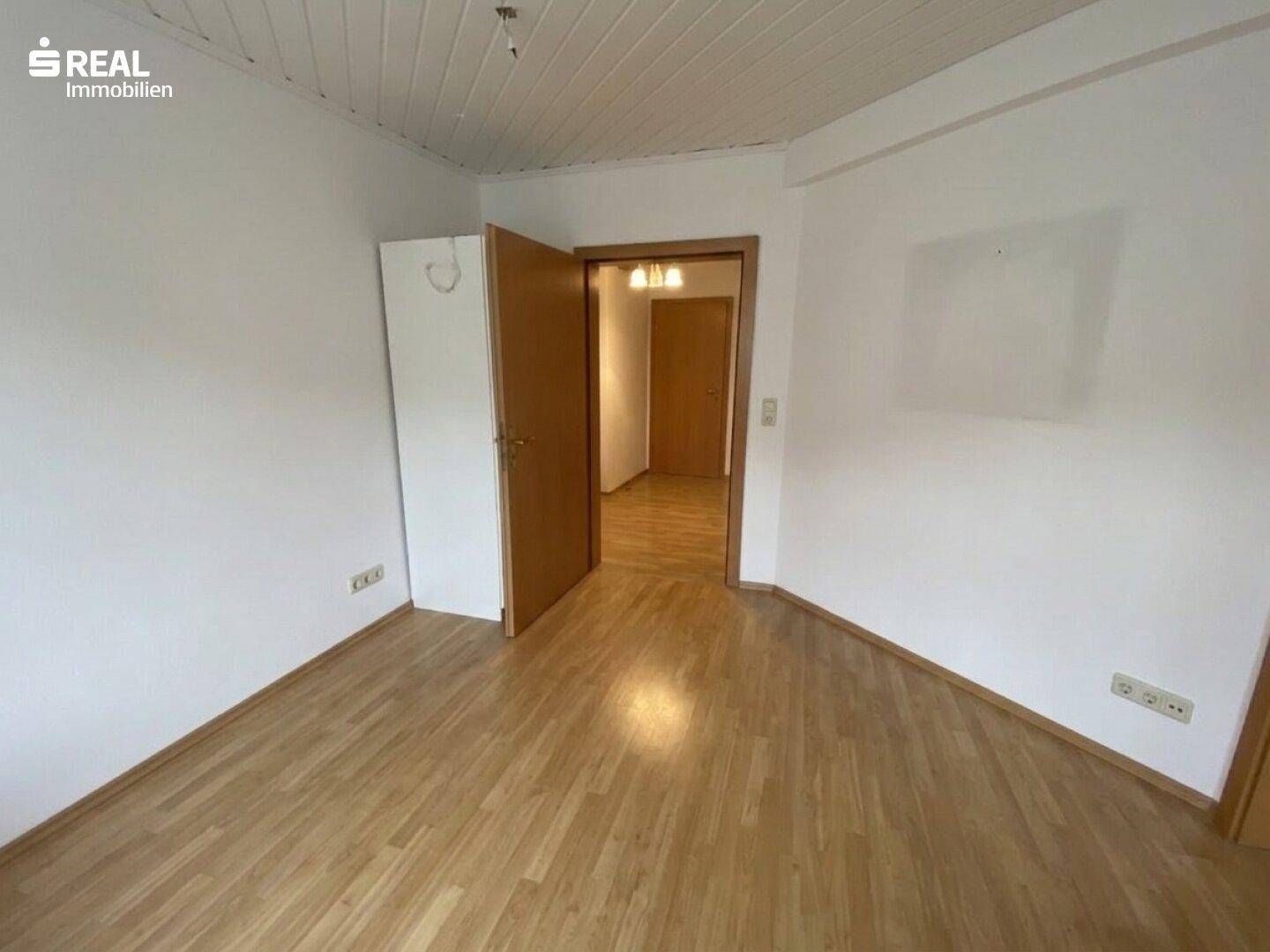 Helles, leeres Zimmer mit Laminatboden und weiß gestrichenen Wänden, bereit zur Einrichtung.