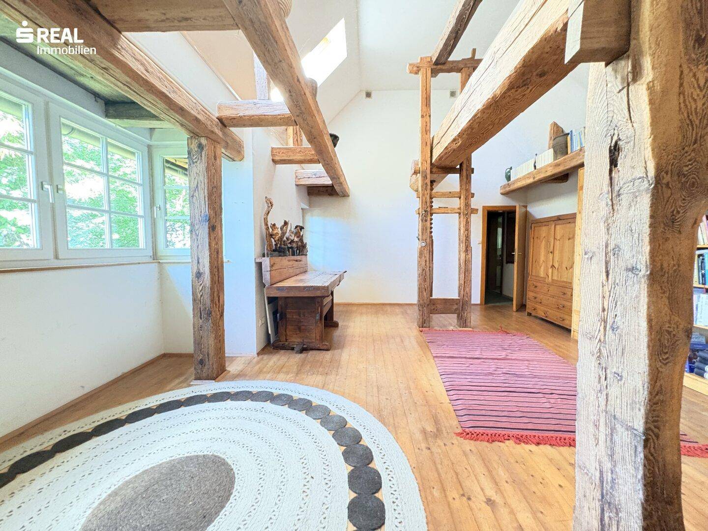Heller Wohnbereich mit freiliegenden Holzbalken, Holzboden und einem runden Teppich.
