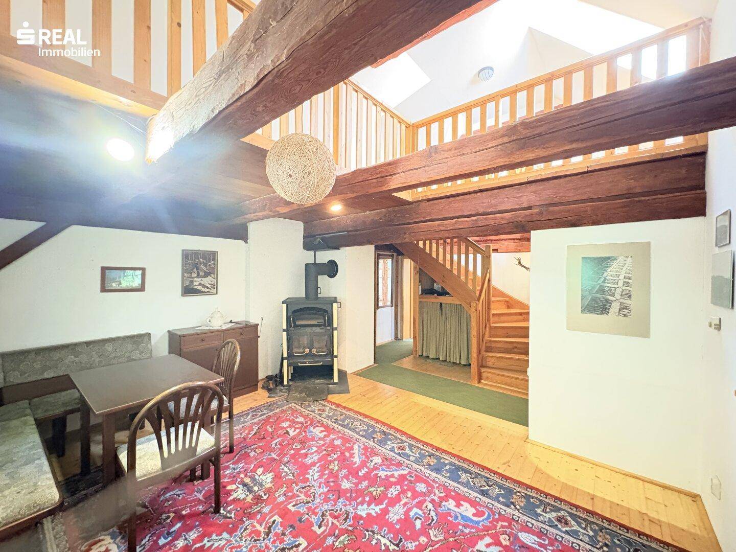 Gemütlicher Wohn-Essbereich mit Holzboden, Kaminofen und einer Holztreppe zur Galerie.