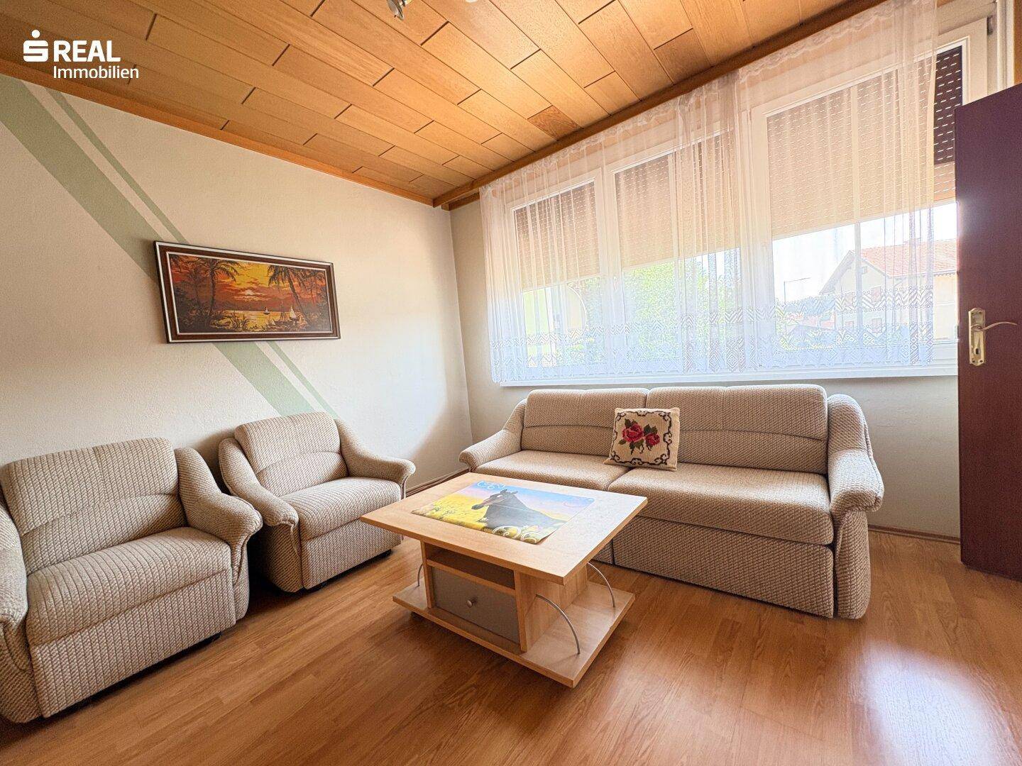 Helles Wohnzimmer mit Holzdecke, Laminatboden und bequemen Sofas.