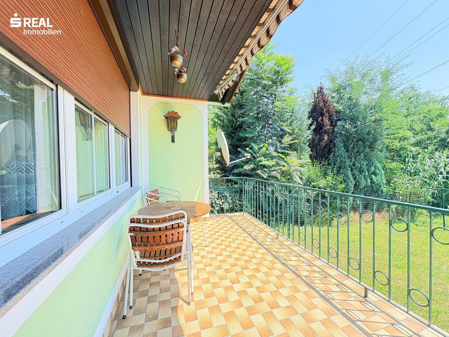 Gemütlicher Balkon mit Fliesenboden und Sitzgelegenheiten, umgeben von viel Grün.