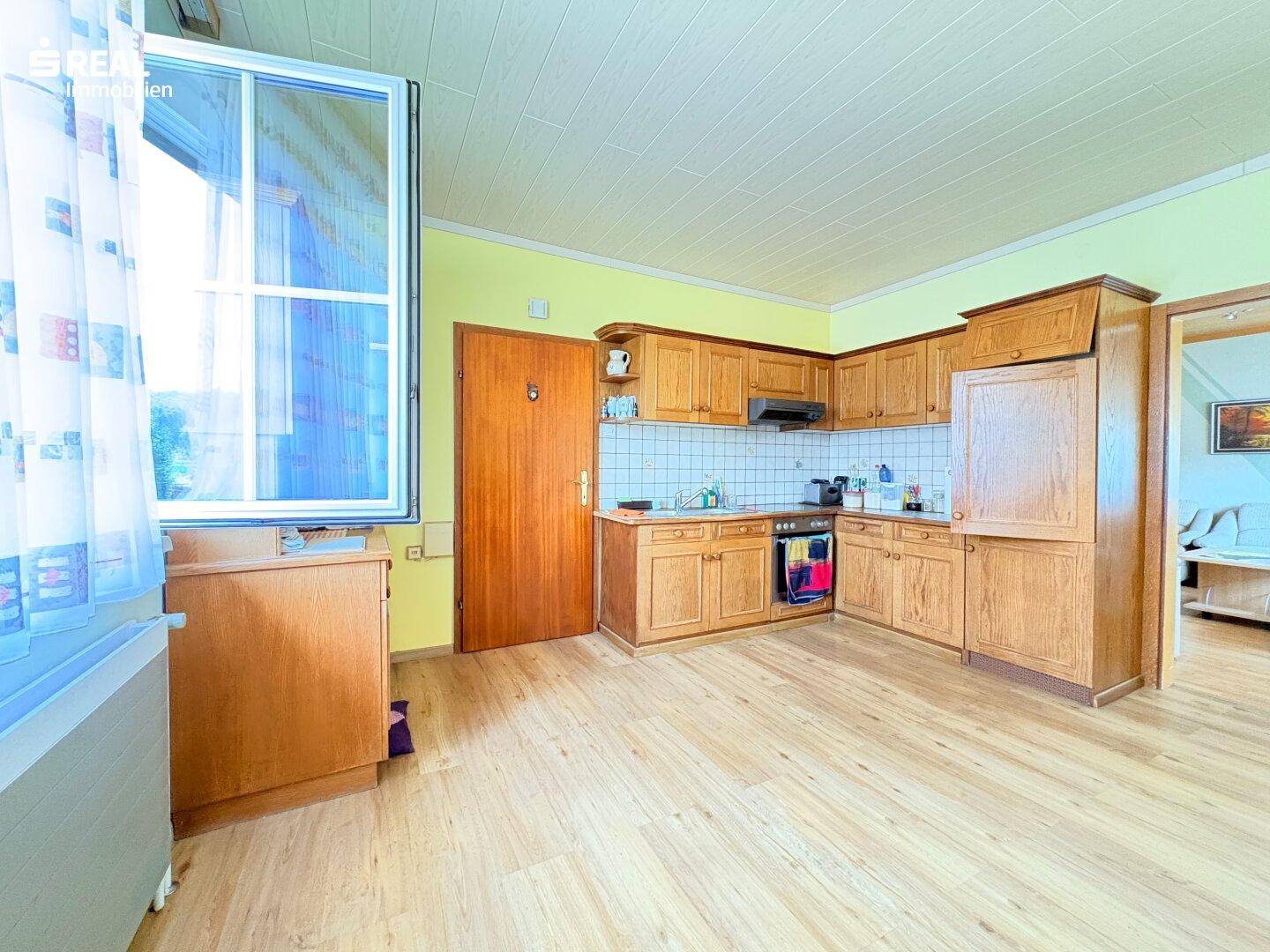 Geräumige Küche mit Holzschränken, Laminatboden und großem Fenster.