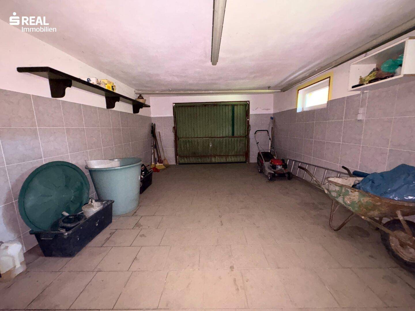 Geräumige Garage mit Fliesenboden und Stauraum für Gartengeräte.