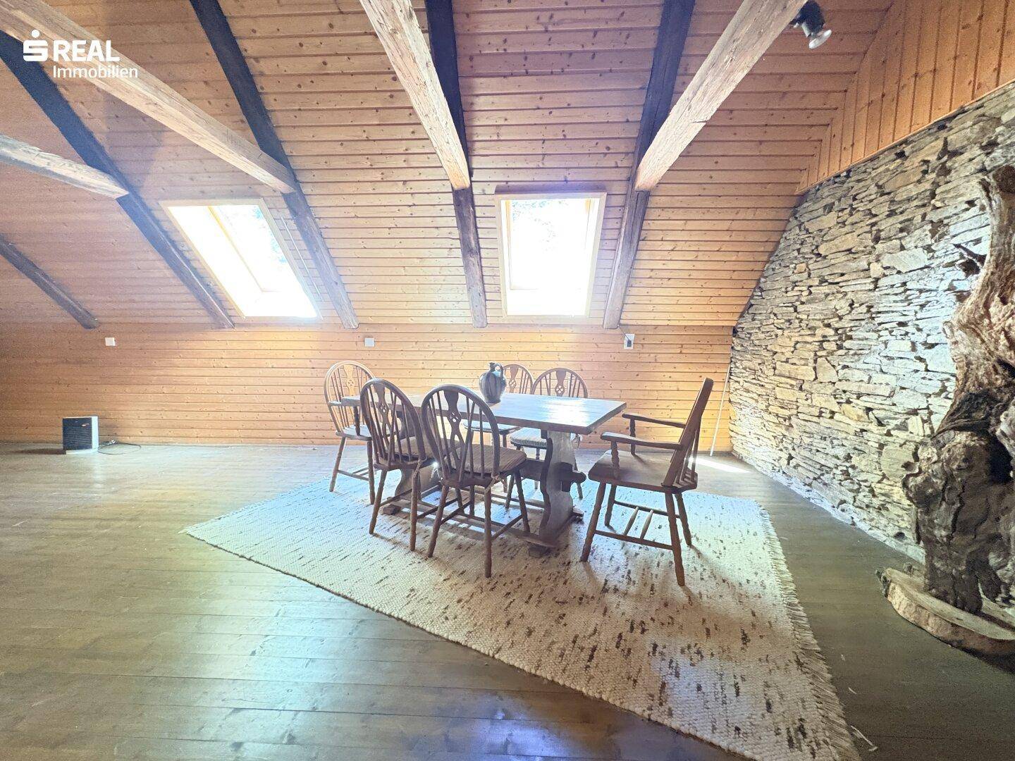 Helles Dachzimmer mit Holztäfelung, Esstisch und Dachfenstern, ideal für gesellige Runden.