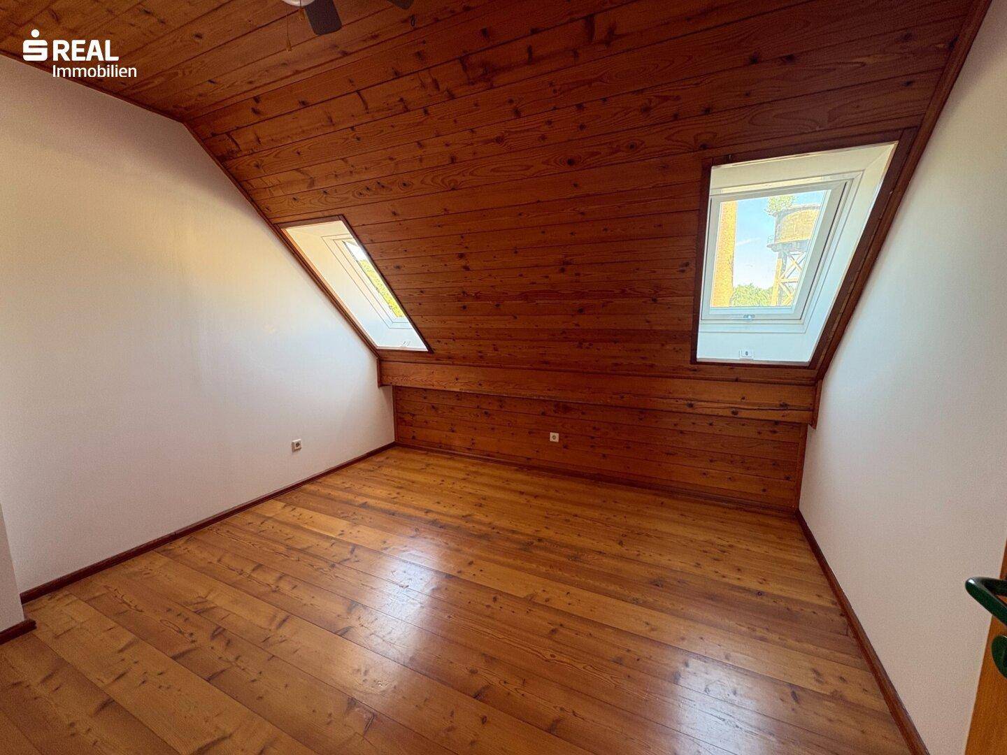 Gemütliches Schlafzimmer im Dachgeschoss mit Holzdecke, Holzboden und zwei Dachfenstern.