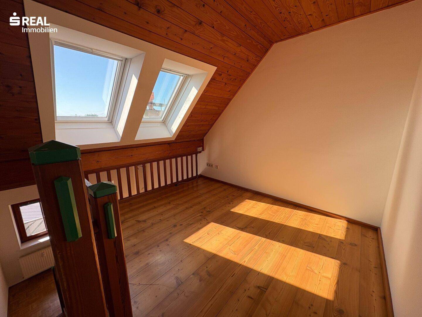 Helle Galerie mit Holzfußboden und Dachfenstern, die viel Tageslicht hereinlassen.