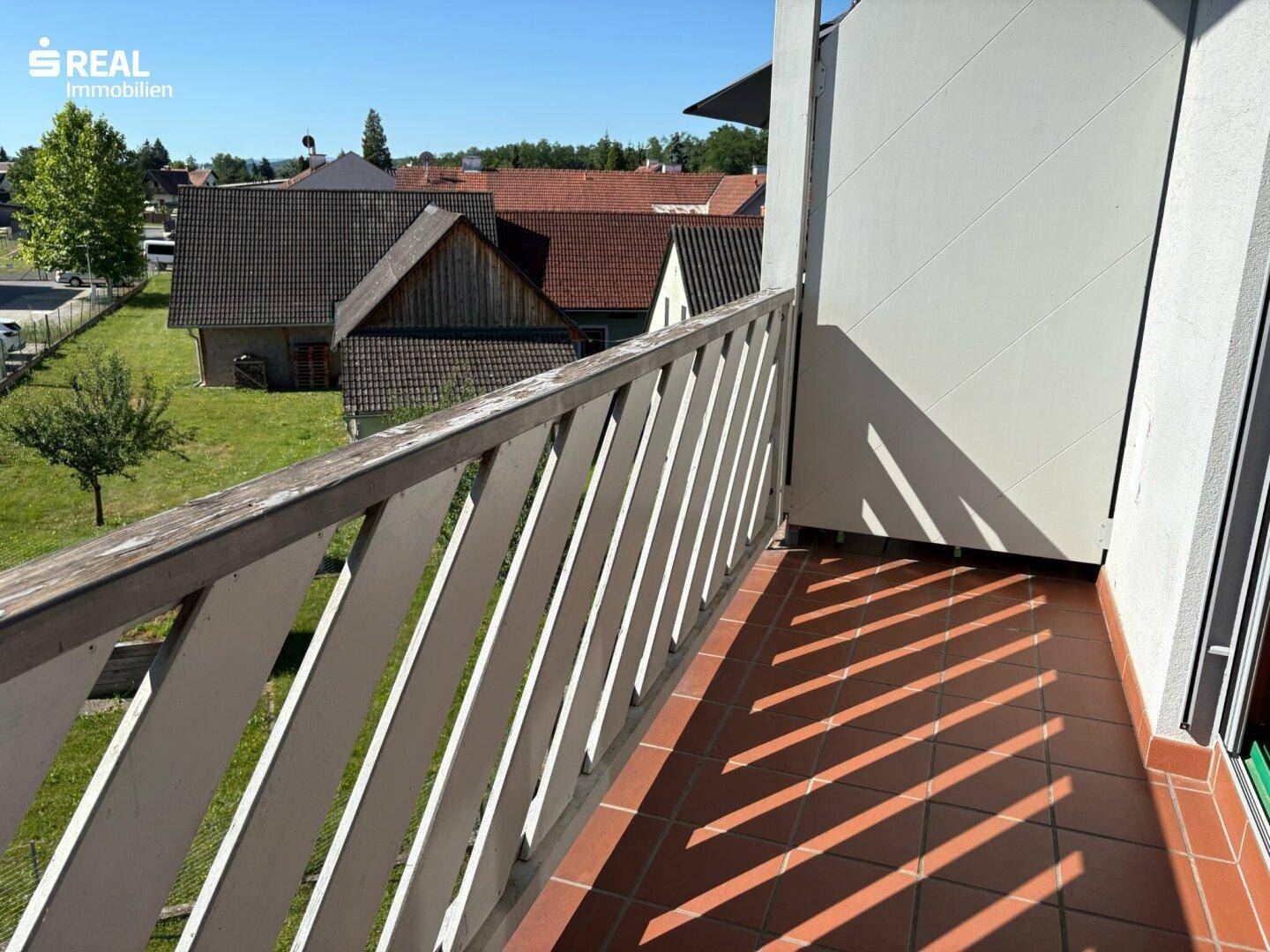 Balkon mit Blick ins Grüne und auf die umliegenden Häuser, gefliestem Boden.