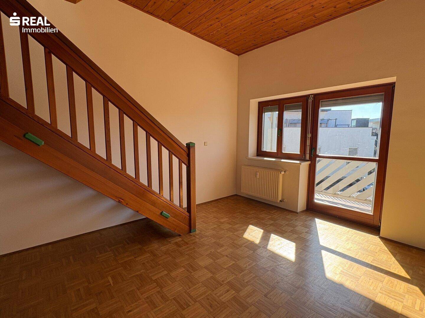 Heller Wohnbereich mit Parkettboden, Holztreppe und Zugang zu einem Balkon.