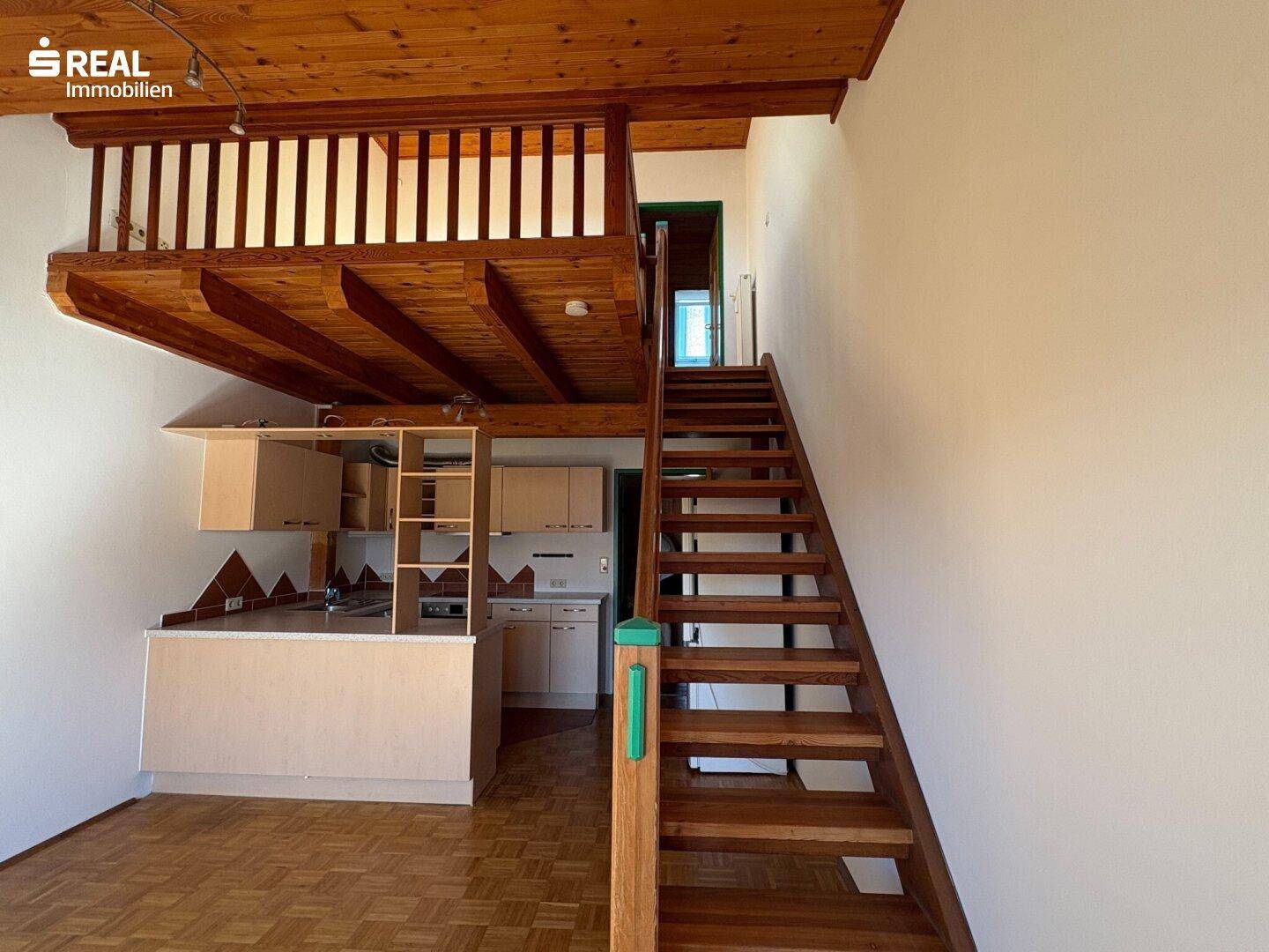 Geräumiger Wohnbereich mit Holztreppe zur Galerie und integrierter Küchenzeile.