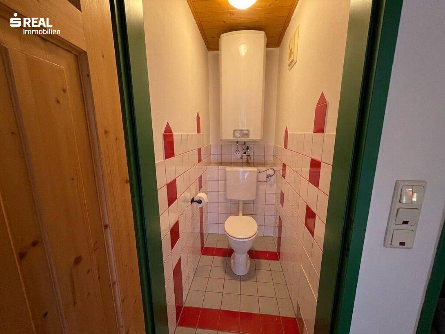 Separate Toilette mit farbigen Fliesen, WC und Warmwasserboiler an der Wand.