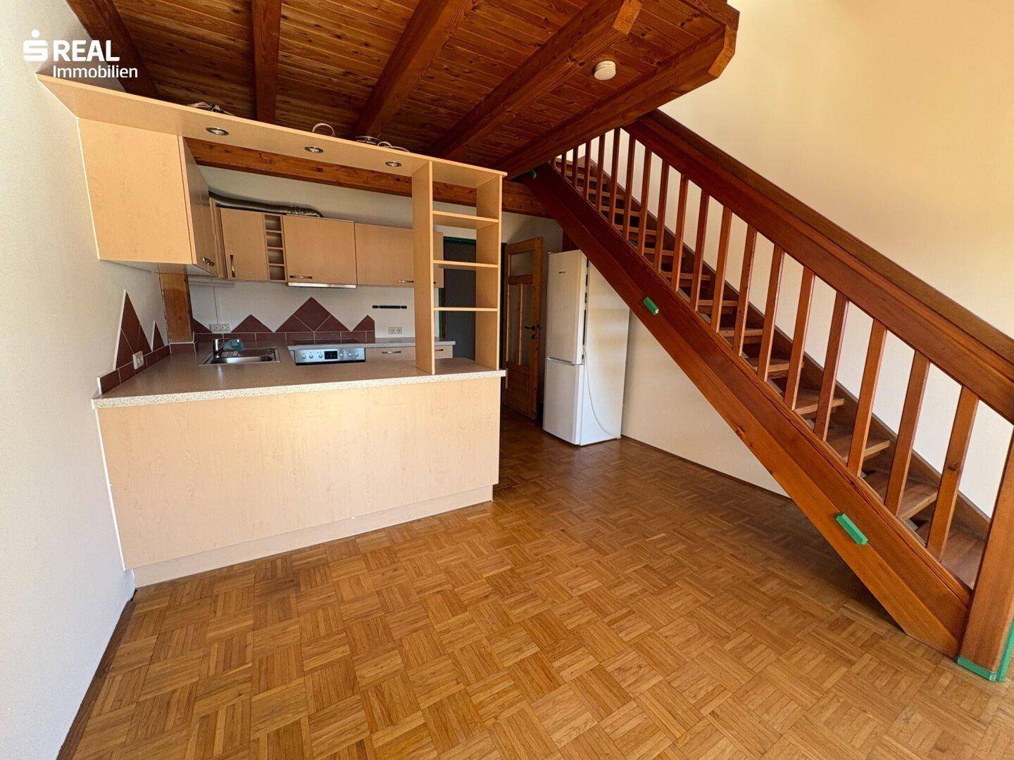Wohnbereich mit integrierter Küchenzeile, Kühlschrank und Holztreppe zur oberen Etage.