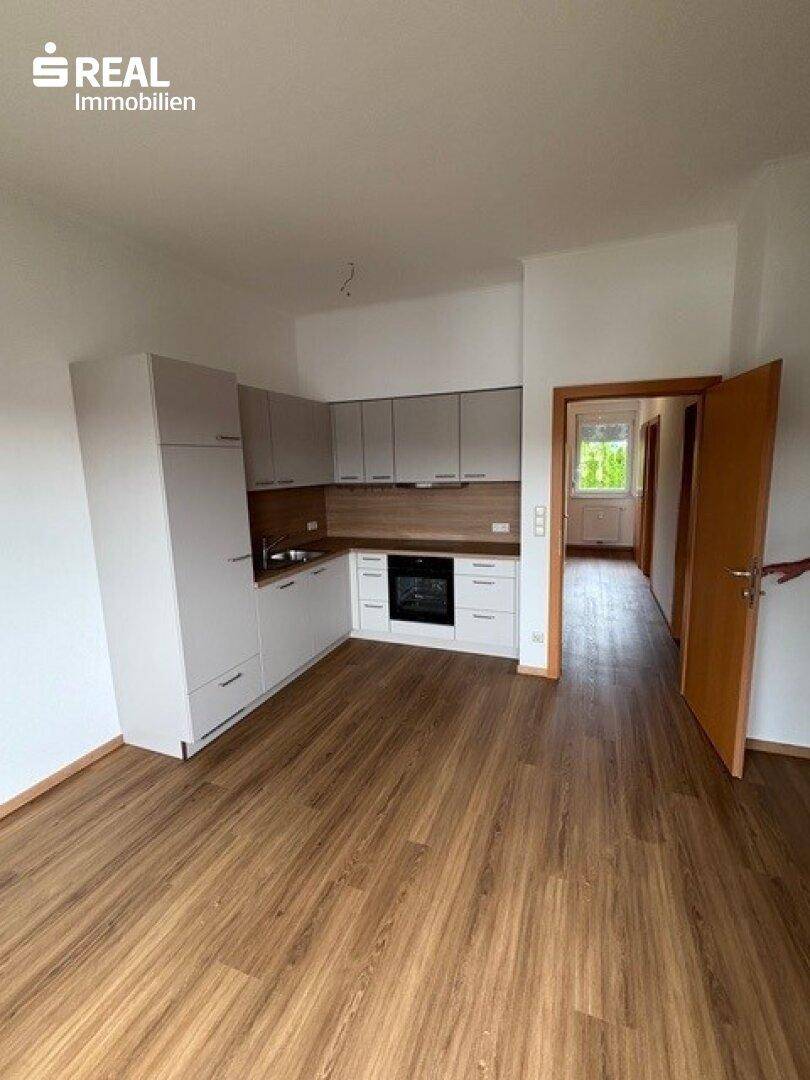 Moderne, helle Küche mit grauen Schränken und Holzarbeitsplatte in einem offenen Wohnbereich.