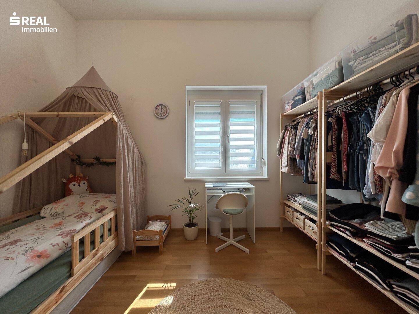 Kinderzimmer mit charmantem Himmelbett, Schreibtisch und offenem Kleiderschrank.
