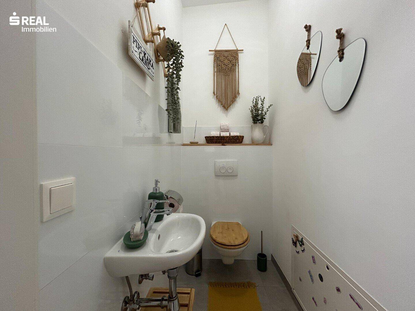 Modernes Gäste-WC mit wandhängender Toilette, kleinem Waschbecken und schlichten Fliesen.
