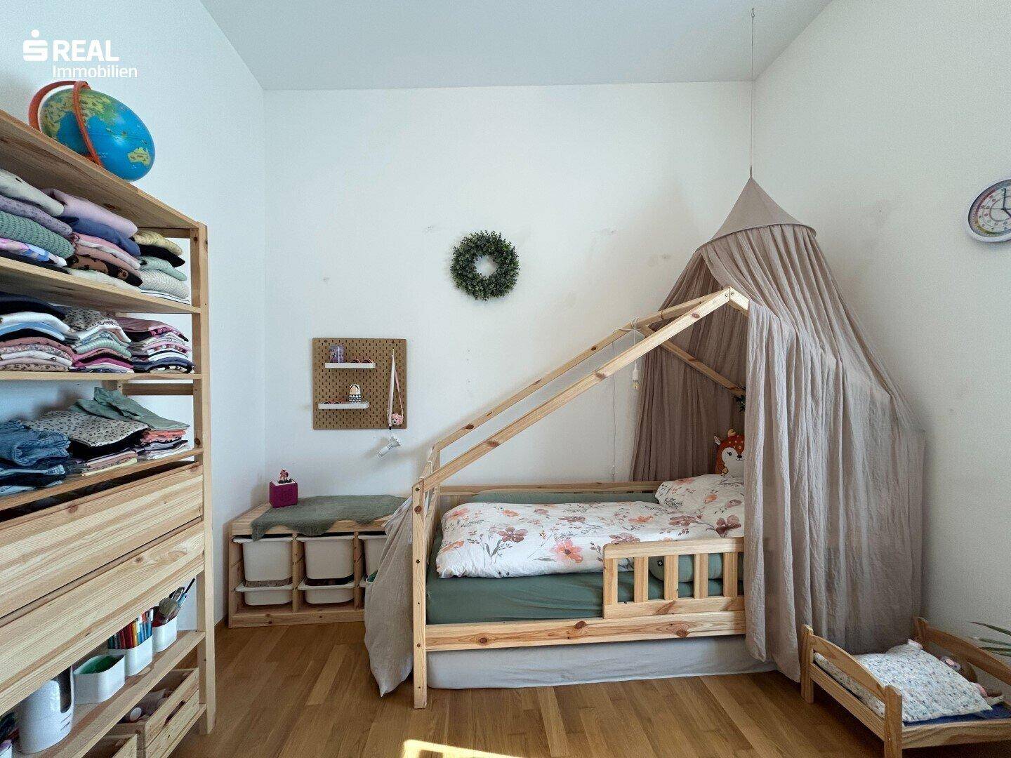Detailansicht des Kinderzimmers mit Holzbett, Baldachin und praktischen Holzregalen.