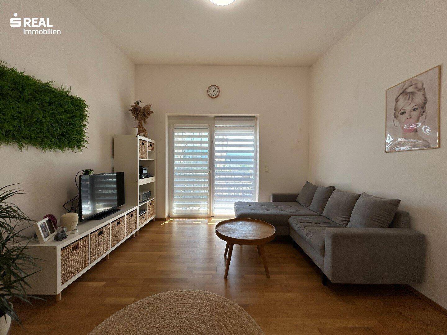 Helles Wohnzimmer mit gemütlichem Ecksofa, Holzboden und Zugang zur Terrasse.