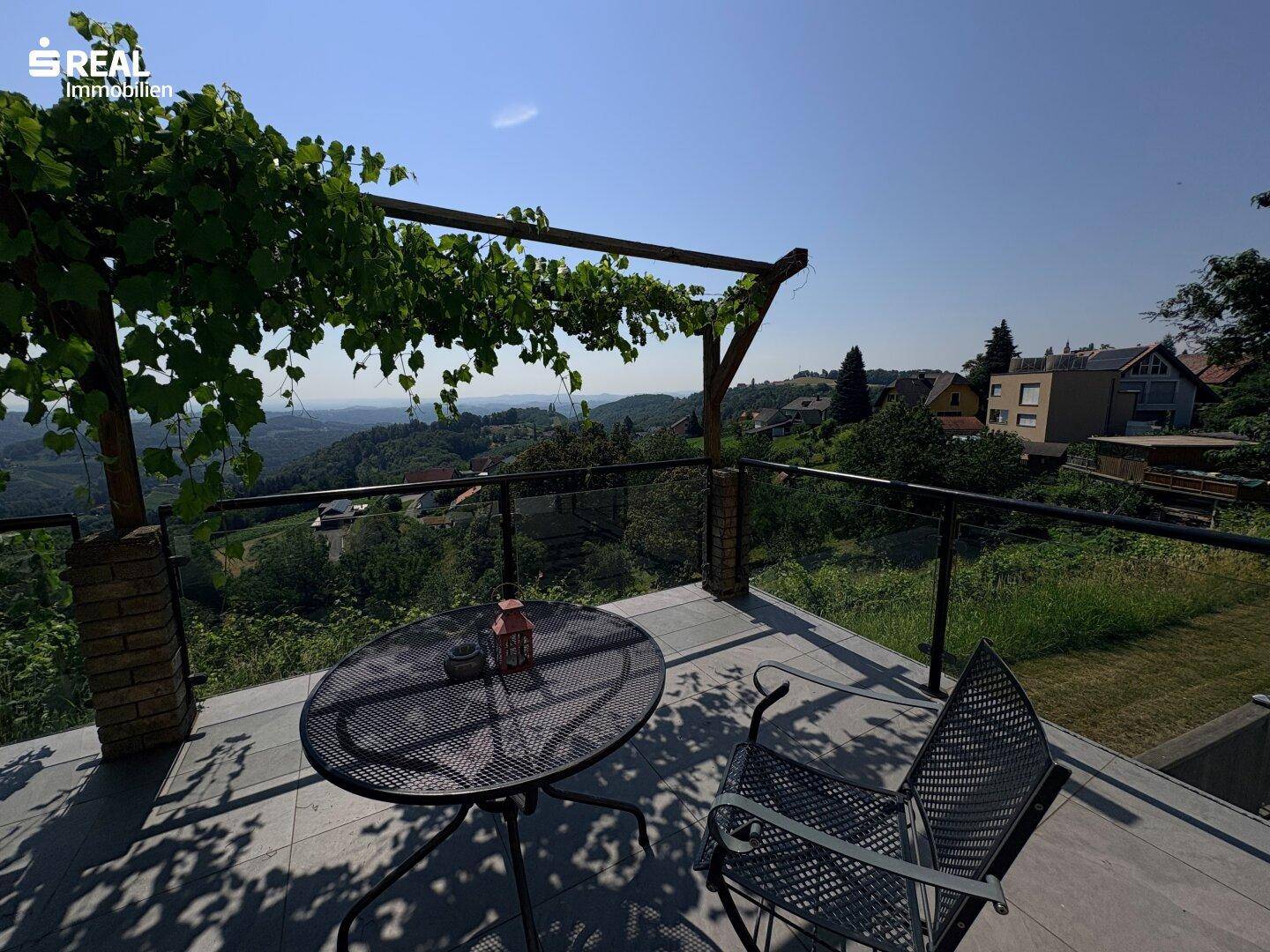 Gemütliche Terrasse mit Pergola und weitem Blick über die hügelige Landschaft unter blauem Himmel.
