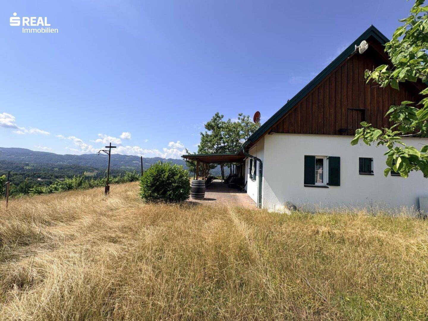 Haus mit weißer Fassade und Holzverkleidung, daneben eine überdachte Terrasse mit Weitblick.