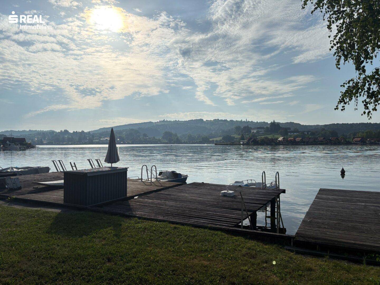 Malerischer Seeblick mit Holzstegen und Booten unter einem sonnigen Himmel.