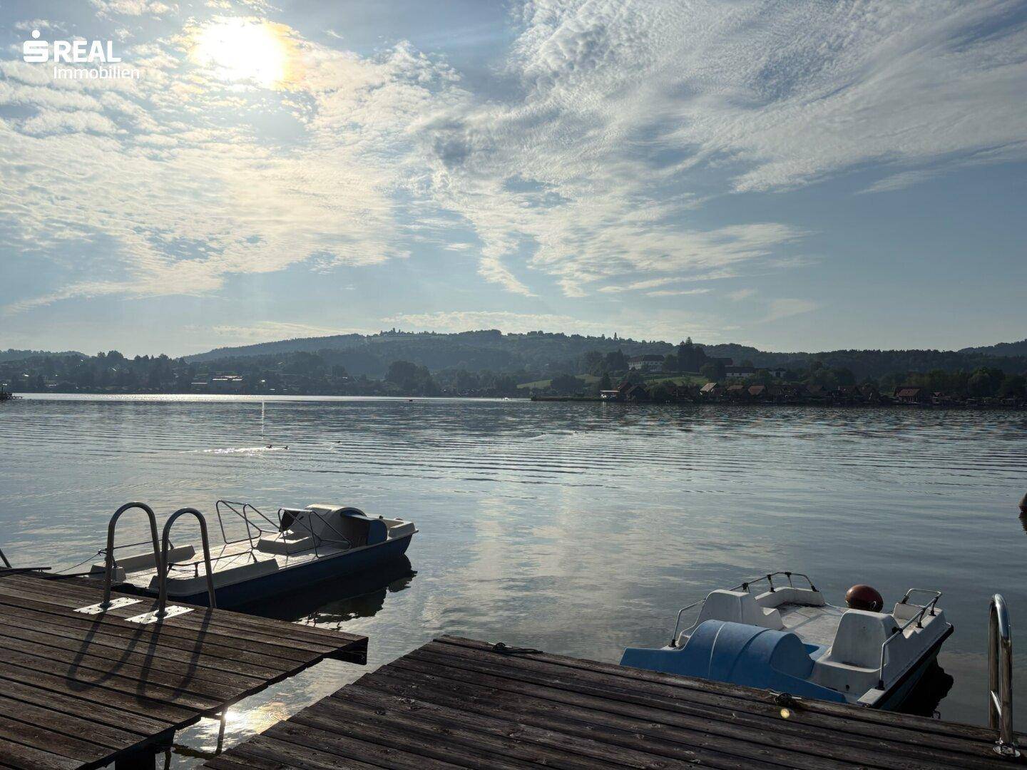 Weitläufiger Blick auf den See mit mehreren Booten und Holzstegen am Ufer.