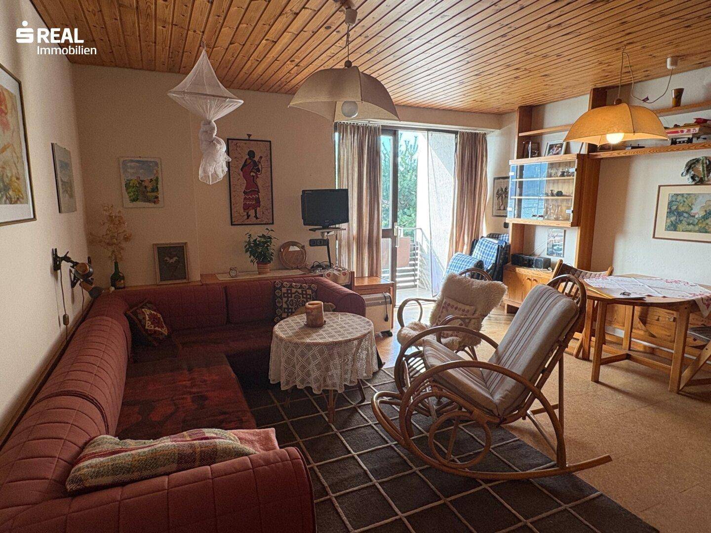 Geräumiges Wohnzimmer mit rotem Sofa, Schaukelstuhl und Zugang zu einem Außenbereich.