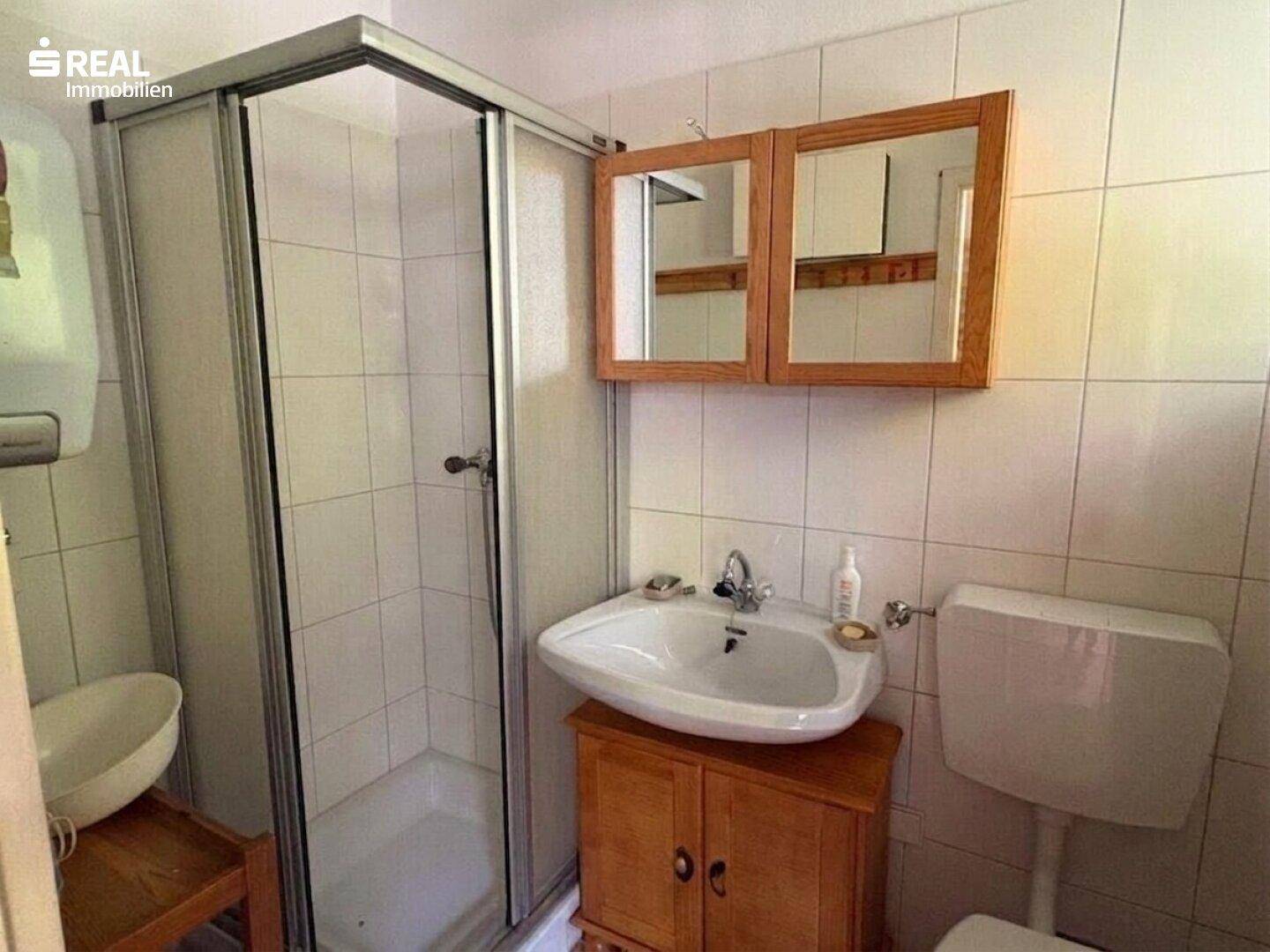 Helles Badezimmer mit Duschkabine, Waschbecken und weißen Fliesen an den Wänden.