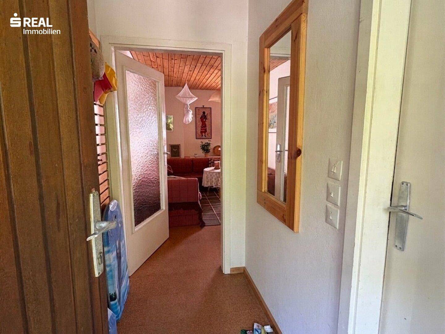 Eingangsbereich mit Holzdetails und einem Spiegel, der zum Wohnbereich führt.
