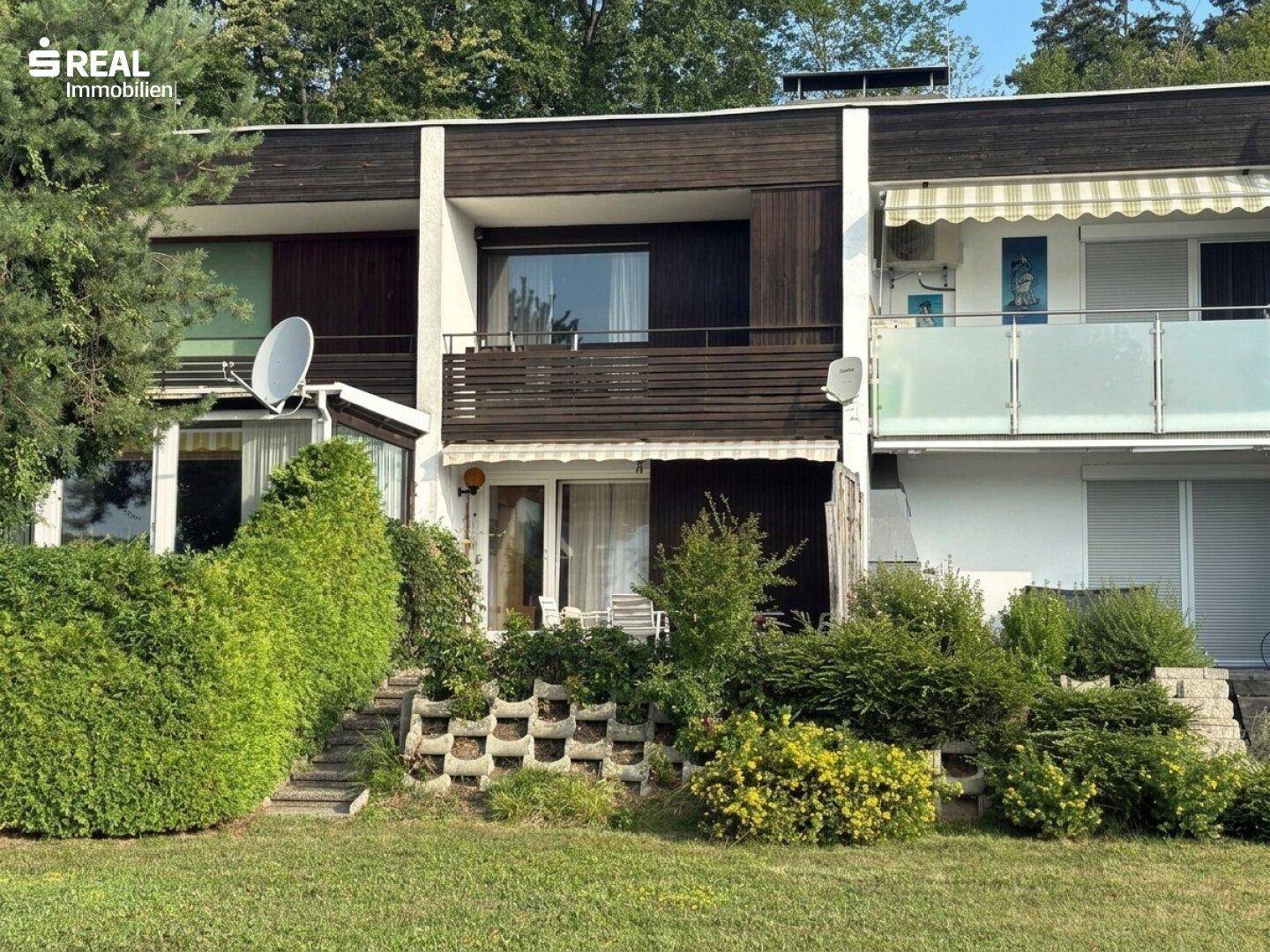 Außenansicht eines Reihenhauses mit gepflegtem Garten, Balkonen und grüner Umgebung.