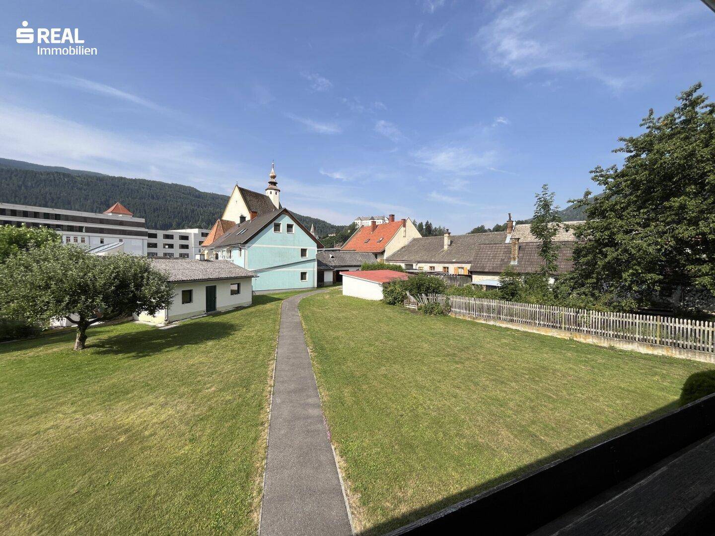 Weitläufiger Gartenbereich mit Blick auf die umliegenden Häuser und die Bergkulisse.