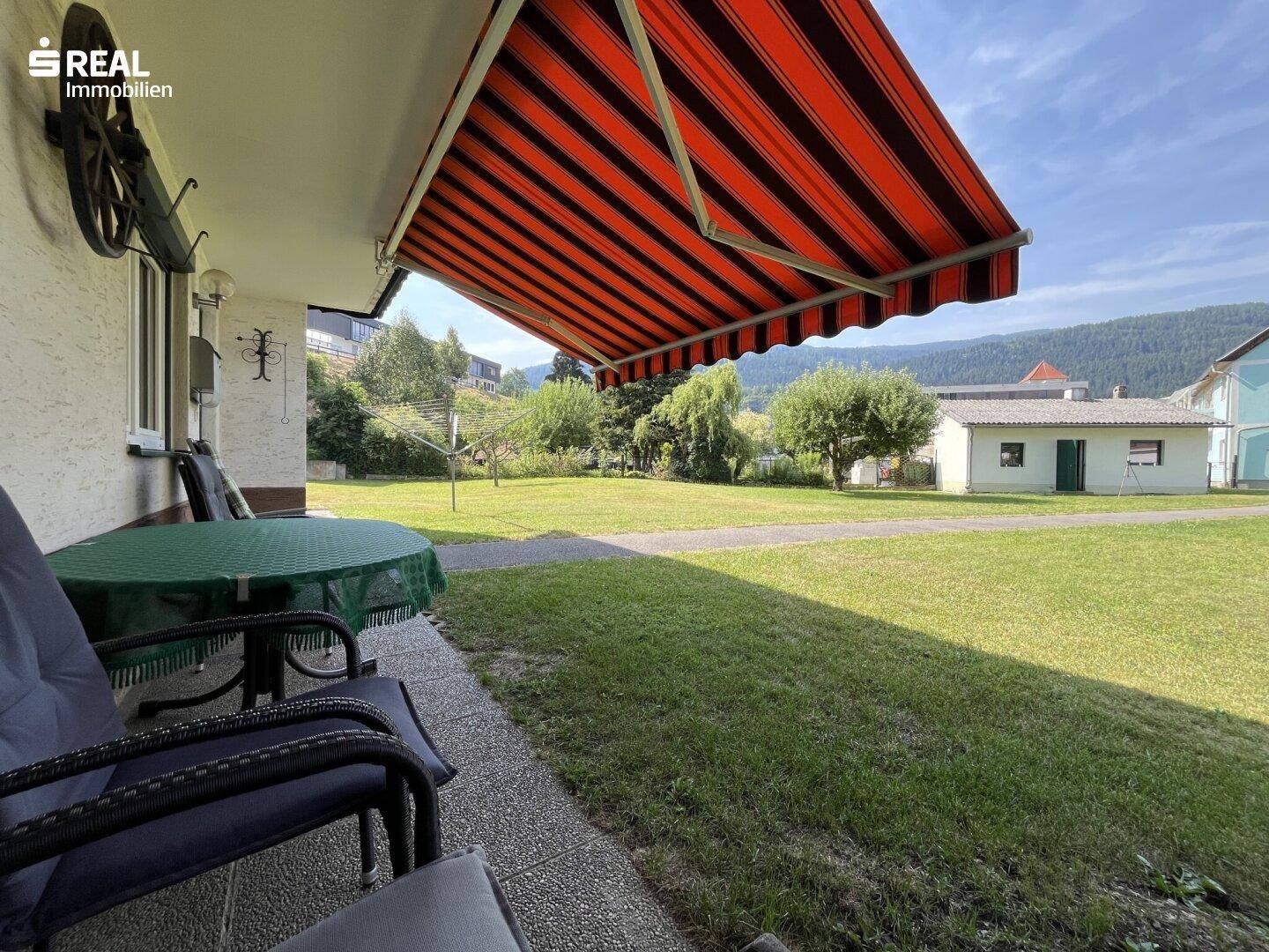 Gemütliche Terrasse mit Markise und Blick auf den weitläufigen grünen Garten.