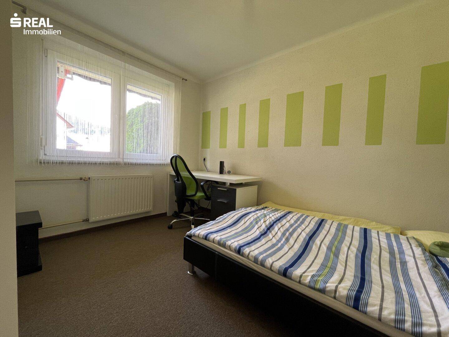 Helles Schlafzimmer mit Einzelbett, Schreibtisch und grün-weiß gestreifter Wand.