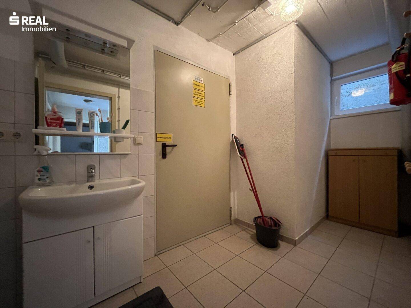 Funktionaler Hauswirtschaftsraum im Untergeschoss mit Waschbecken, Spiegel und Fliesenboden.