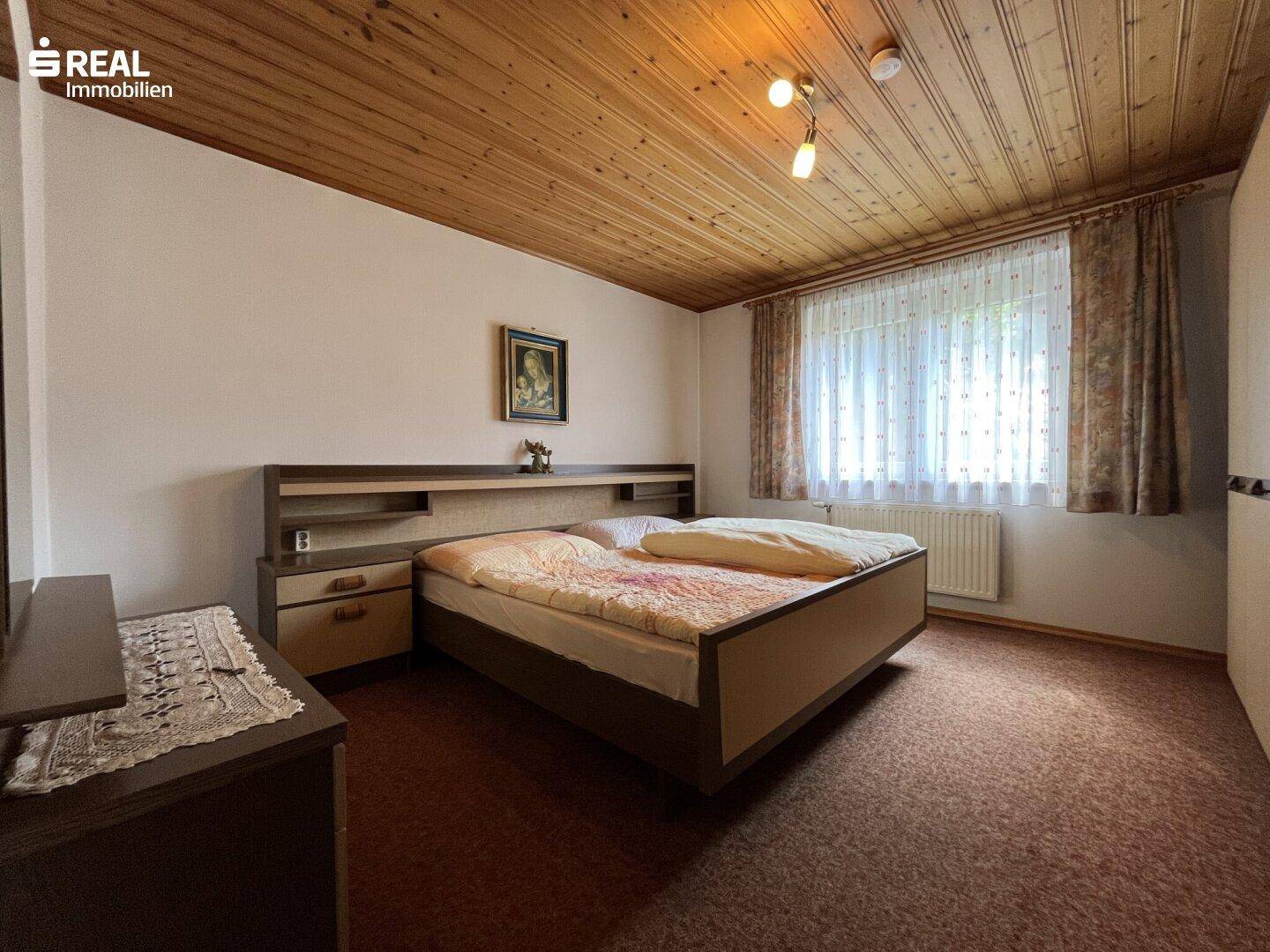 Gemütliches Schlafzimmer mit Doppelbett, Teppichboden und Holzdecke.